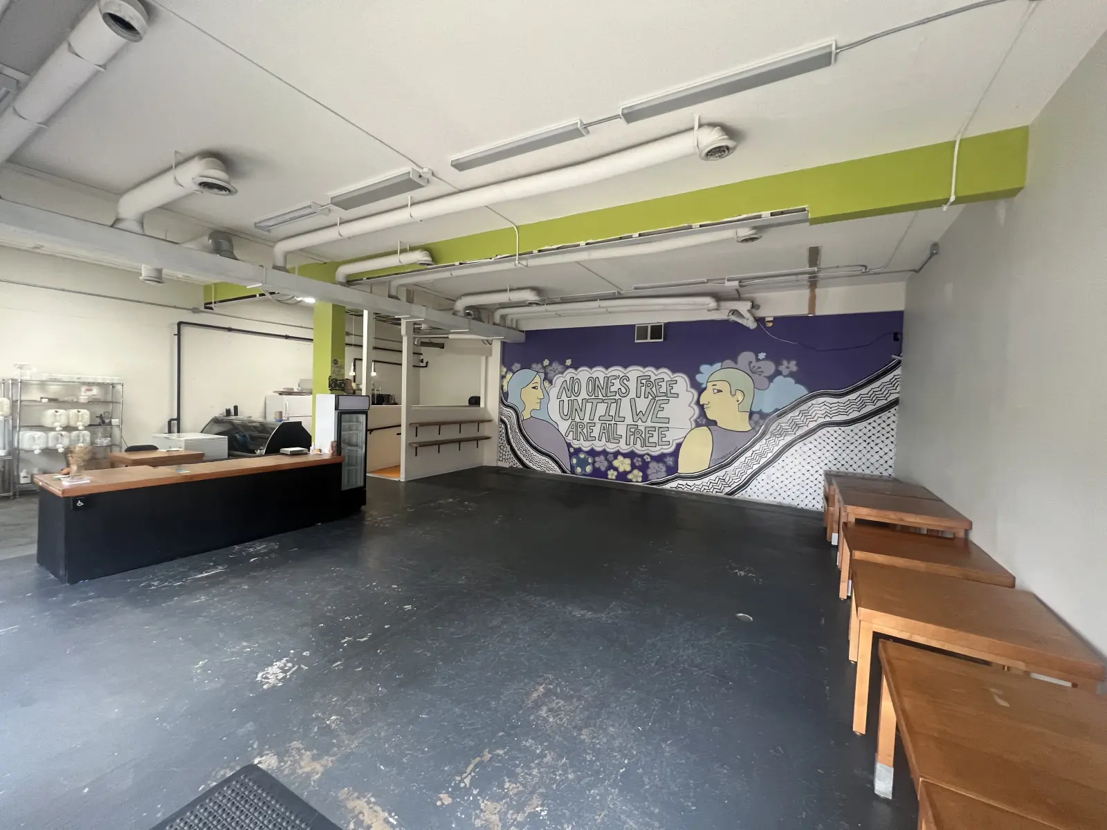 The front room at 206 Piccadilly: a counter, wooden benches and a mural reading no one is free until we are all free