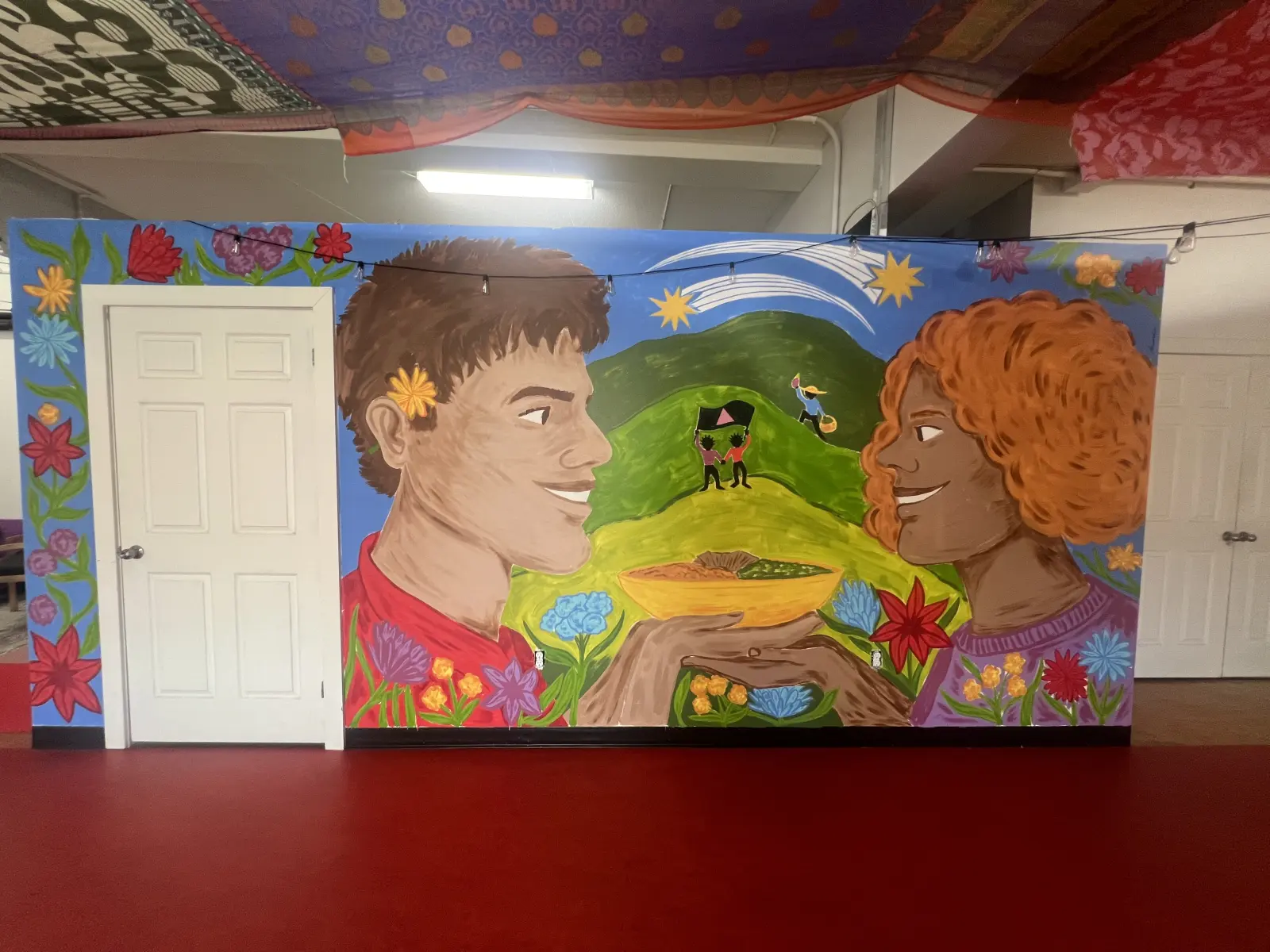 A large painted mural of two figures holding a bowl of flowers, on the wall of the room